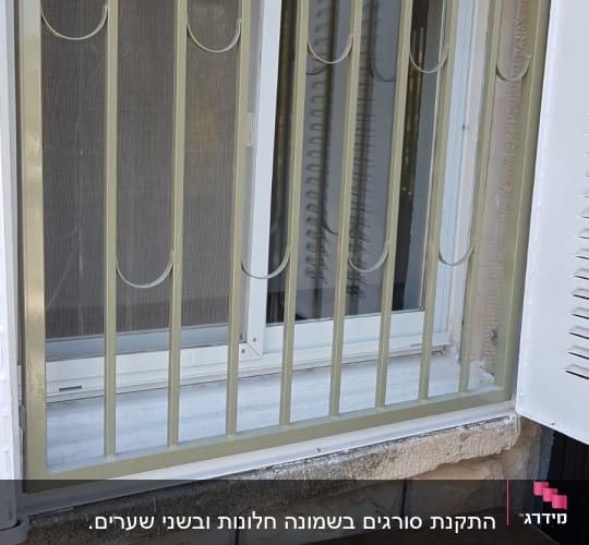 סורגי מתכת על חלון עם מסגרת לבנה